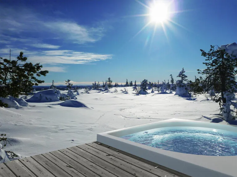 Outdoor-Whirlpool auf einer Holzterrasse in verschneiter Landschaft bei Sonne