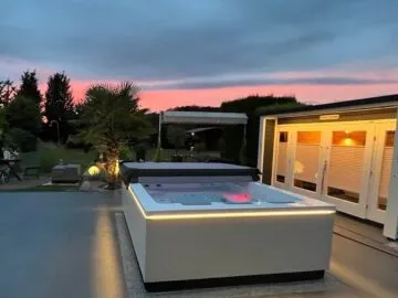 Infinitas Whirlpool The Grand am Abend mit optionaler U-LED Beleuchtung, rechts die Gartensauna